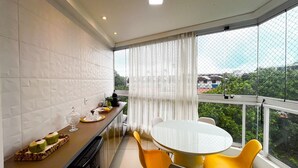 Un balcón con mesa y sillas, una zona de cocina y vistas a zonas verdes y edificios.