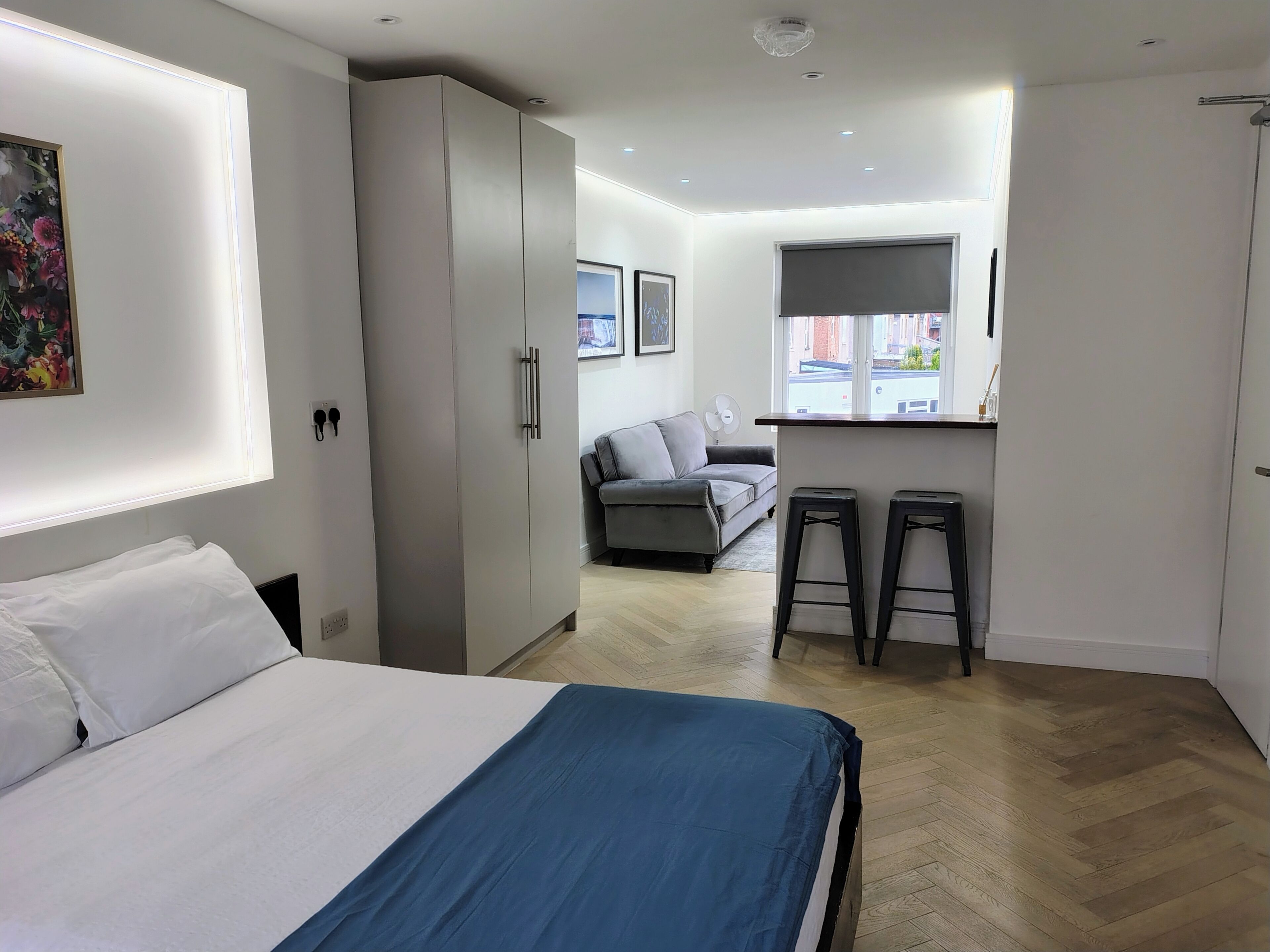 A modern bedroom with a bed, wardrobe, and a kitchenette area with stools.