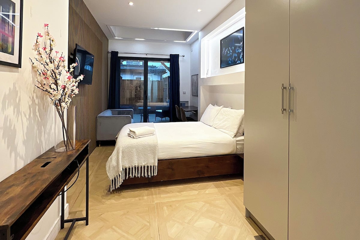 Ein Schlafzimmer mit Bett, Kleiderschrank, Schreibtisch, Stuhl, Fernseher und einem Fenster mit Vorhängen.