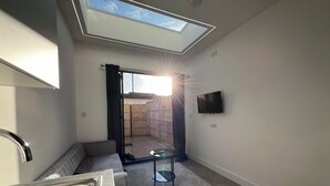 A compact room with a skylight, a flat-screen TV, a sofa, a small table, and a sink.