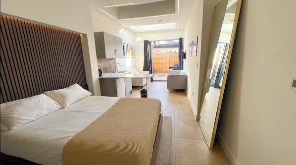 A modern hotel room with a large bed, a small desk, a mirror, and a view of the outside.