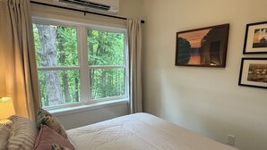 Ein Schlafzimmer mit einem Bett, einem Fenster mit Vorhängen und zwei gerahmten Bildern an der Wand.