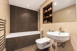Ein Badezimmer mit Badewanne, Toilette und Waschbecken, mit dunklen Fliesen und Holzregalen.