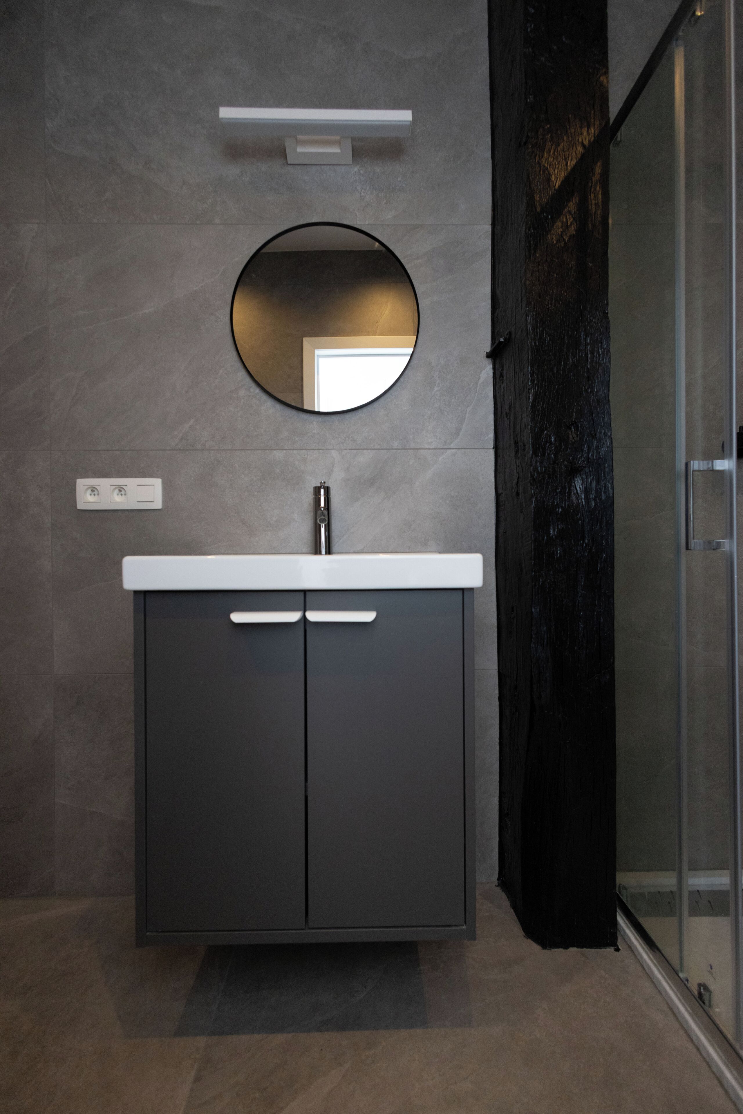Een moderne badkamer met een ronde spiegel, een wit aanrecht en een donker kastje.