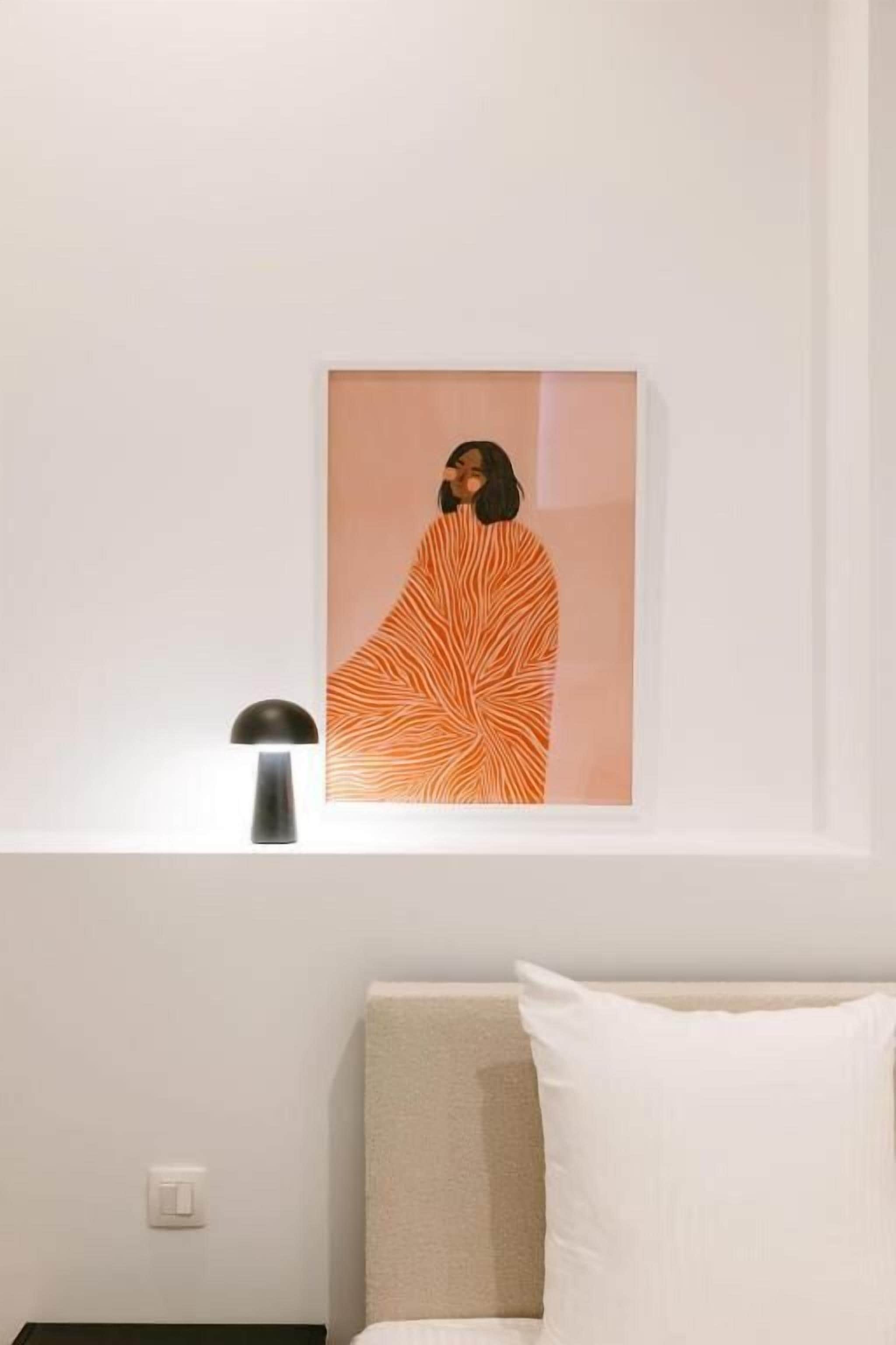 Een lijstwerk aan de muur, een bedlampje en een bed met een kussen.