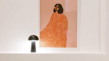 Een lijstwerk aan de muur, een bedlampje en een bed met een kussen.