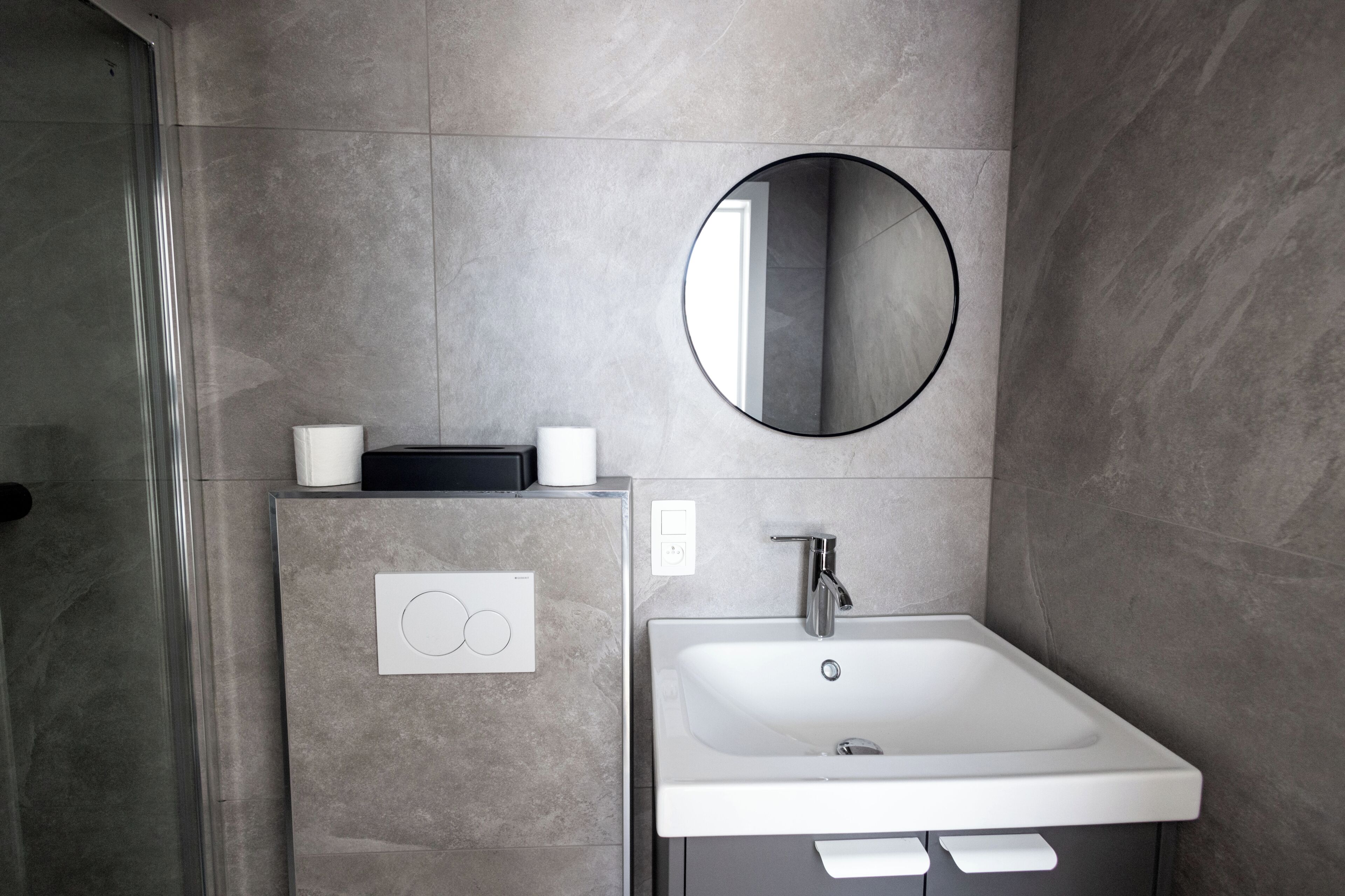 Een moderne badkamer met een witte wastafel, een ronde spiegel en een handdoekhouder.