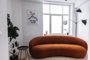A modern living room with a curved sofa, a small round table, a floor lamp, and a window with a view.