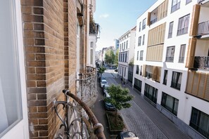 A narrow urban street with buildings on either side, a visible balcony with a metal railing, and a tree in the foreground. - Maison Béguinage Brussels (Brussels)