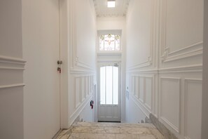 Un couloir avec une porte blanche, un vitrail et un sol en marbre.