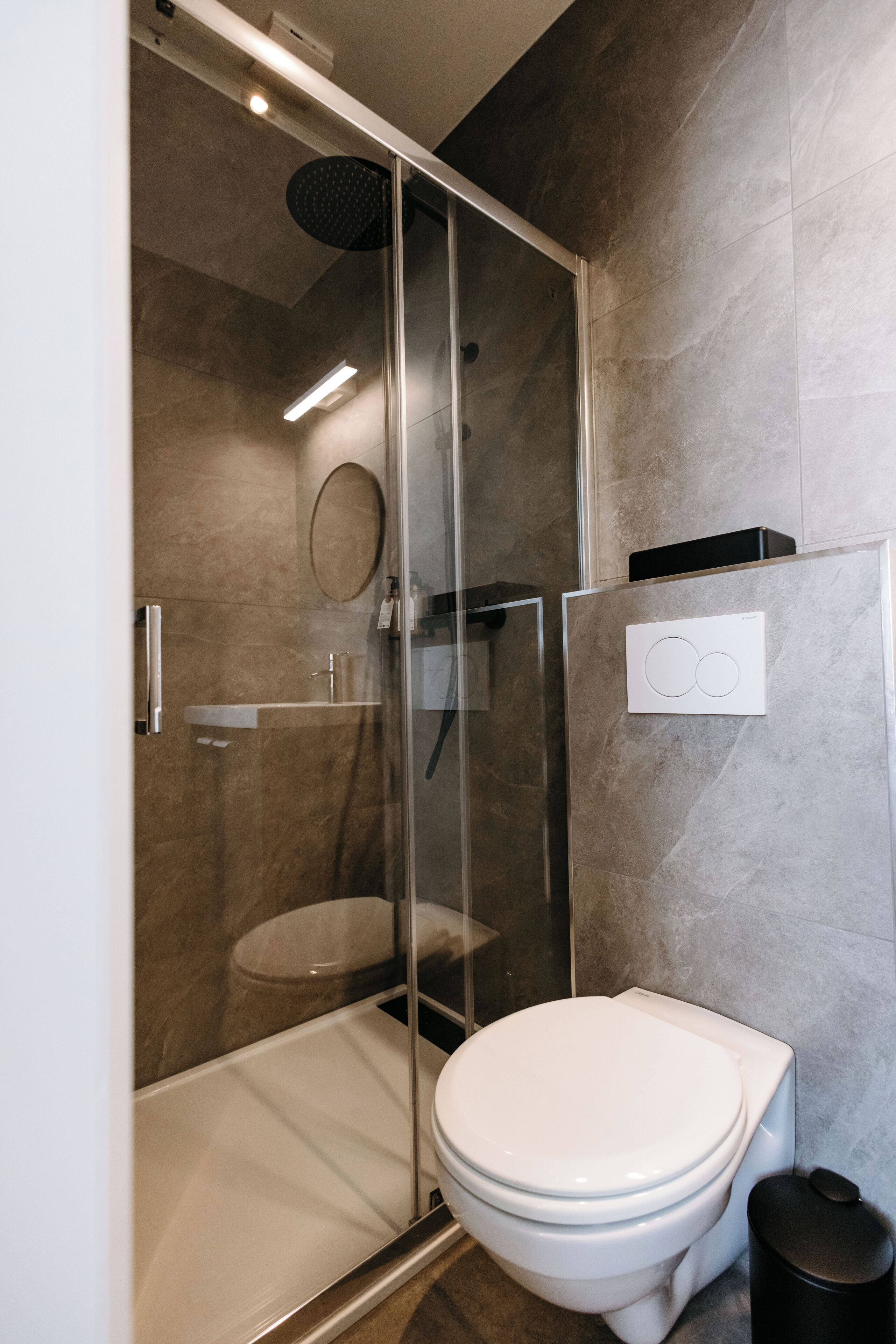 Un baño moderno con ducha de vidrio, inodoro blanco y panel de control en la pared.