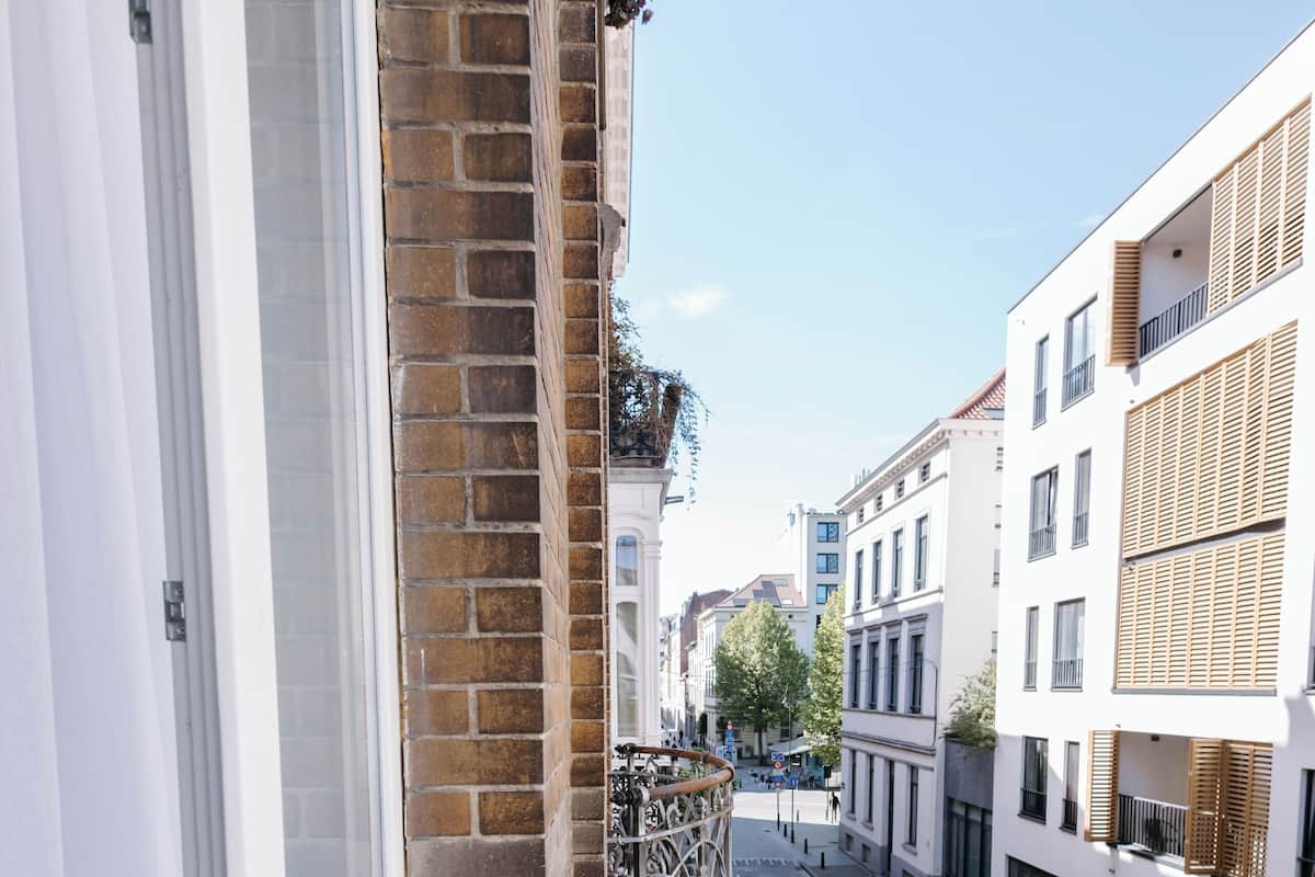 Un balcon doté d’une balustrade en fer forgé, d’un mur en briques et offrant une vue sur une rue bordée d’immeubles.