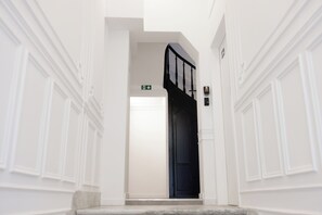 Un couloir aux murs blancs, une porte noire et un sol en marbre.