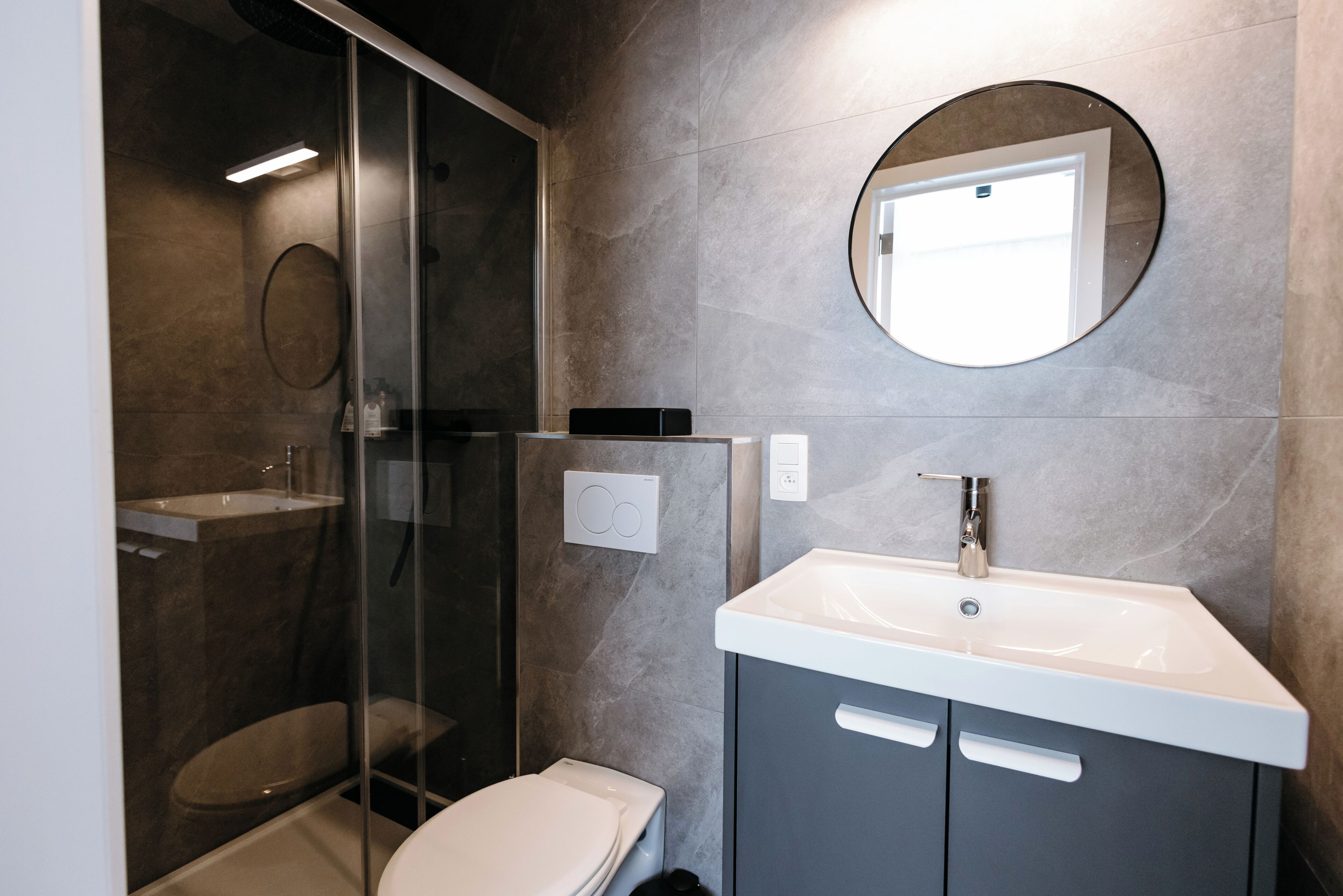 A modern bathroom with a glass-enclosed shower, a white toilet, a sink with a mirror above it, and a cabinet below.