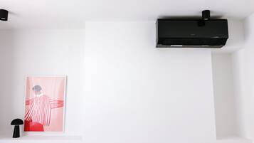 A white room with a black air conditioning unit, a framed abstract painting, and a black floor lamp.
