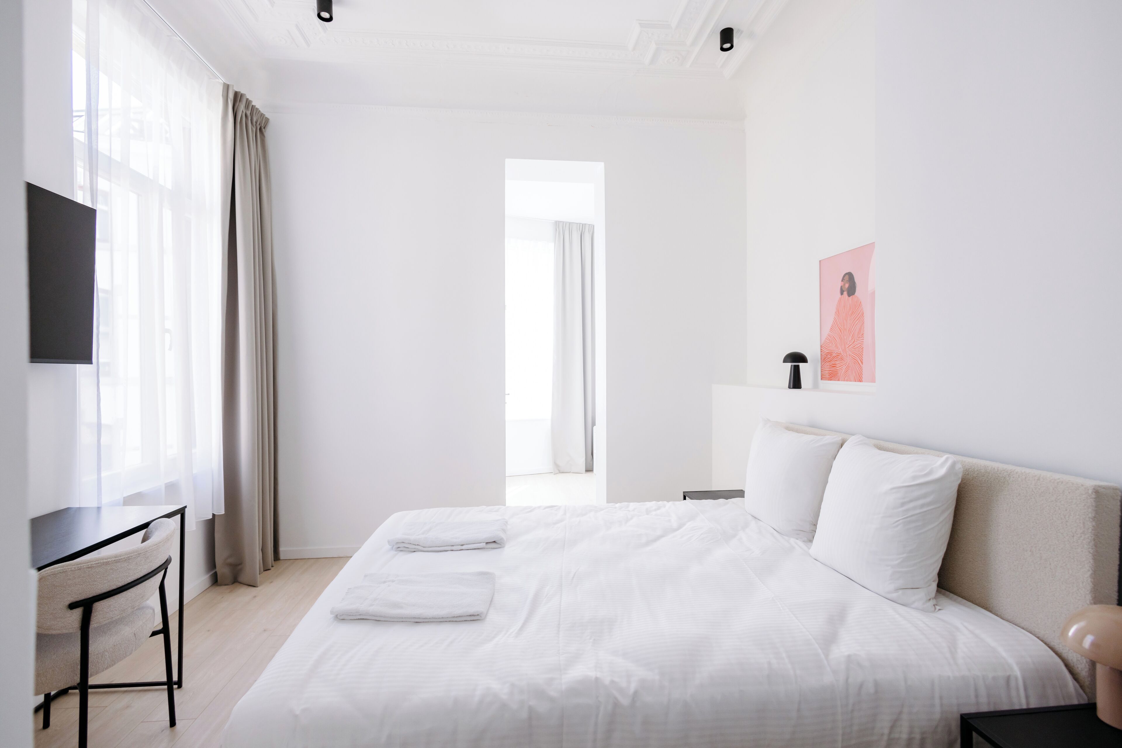 A hotel room with a bed, a desk, a chair, a TV, and a painting on the wall.