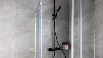 A glass-enclosed shower area with a handheld showerhead, a wall-mounted faucet, and two bottles of shampoo.