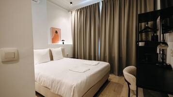 Habitación de hotel con cama, escritorio, silla, lámpara y ventana con cortinas.