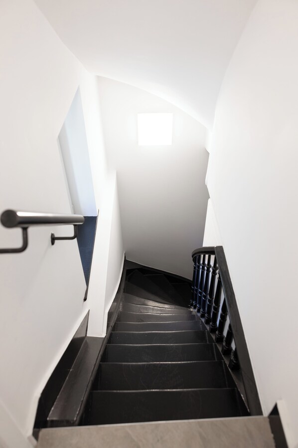 A staircase with a handrail, black steps, and a light source at the top. - Maison Béguinage Brussels (Brussels)