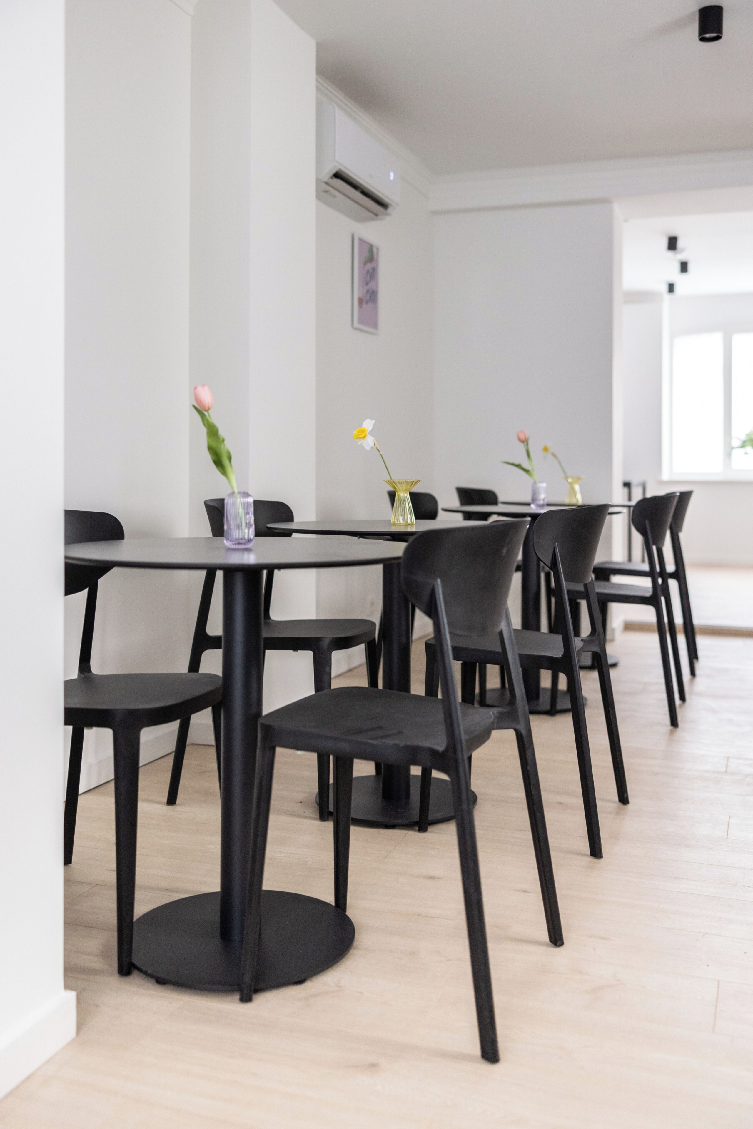 Un comedor moderno con mesas redondas y sillas negras, que presenta un diseño minimalista y un suelo de madera clara.