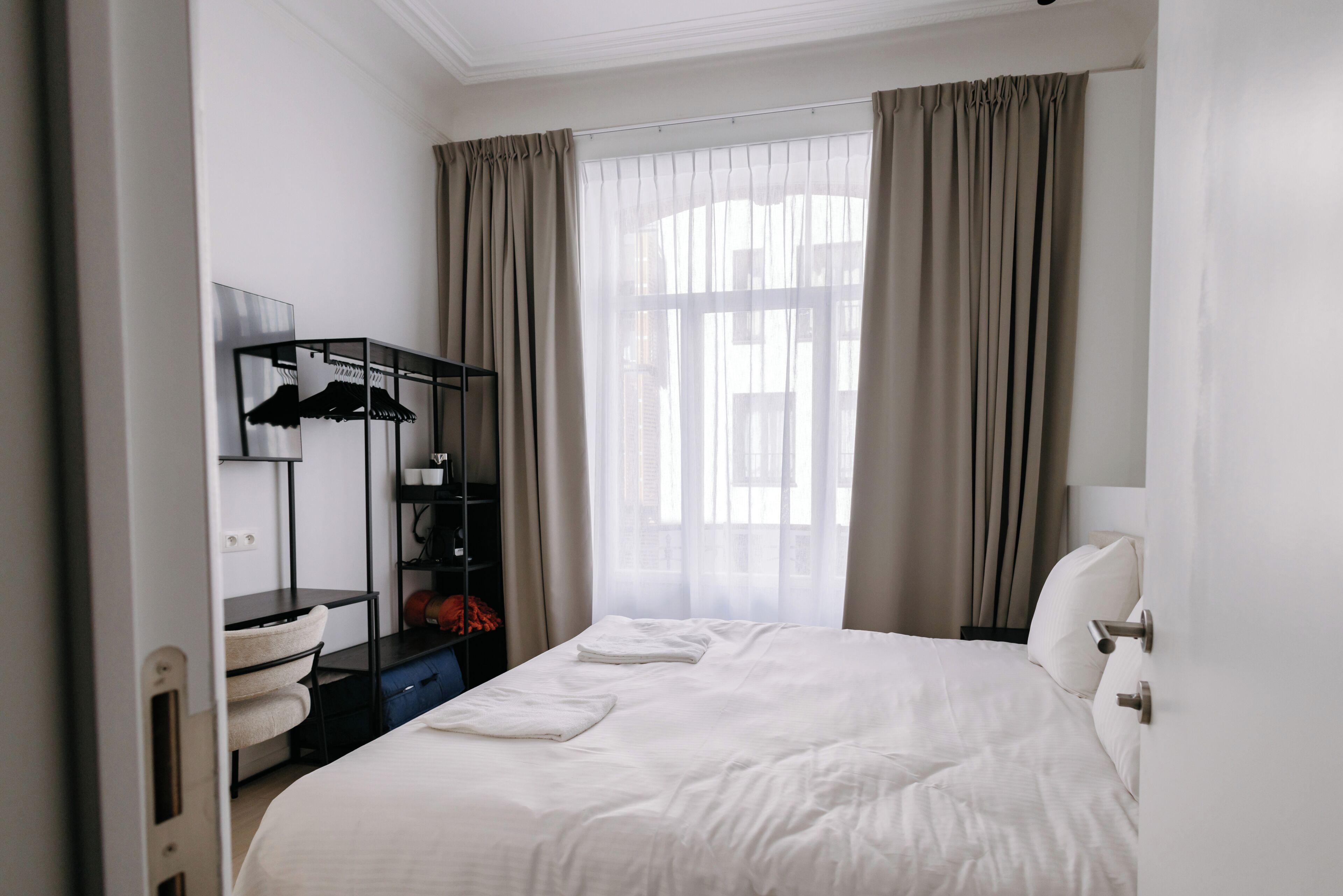A hotel room with a bed, a wardrobe, a mirror, and a window with curtains.