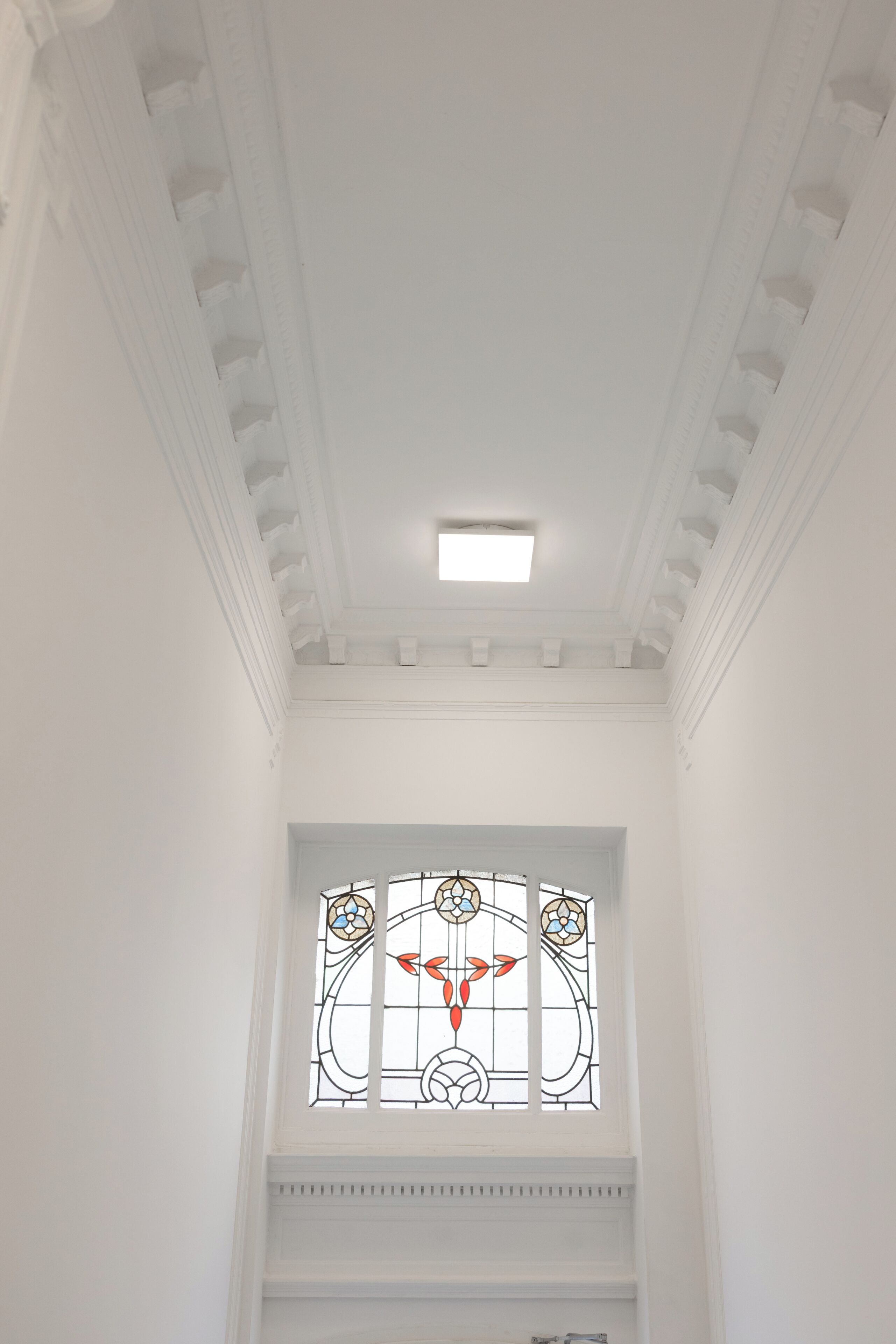 Un intérieur blanc avec un luminaire au plafond, une fenêtre à vitraux et un mur blanc.
