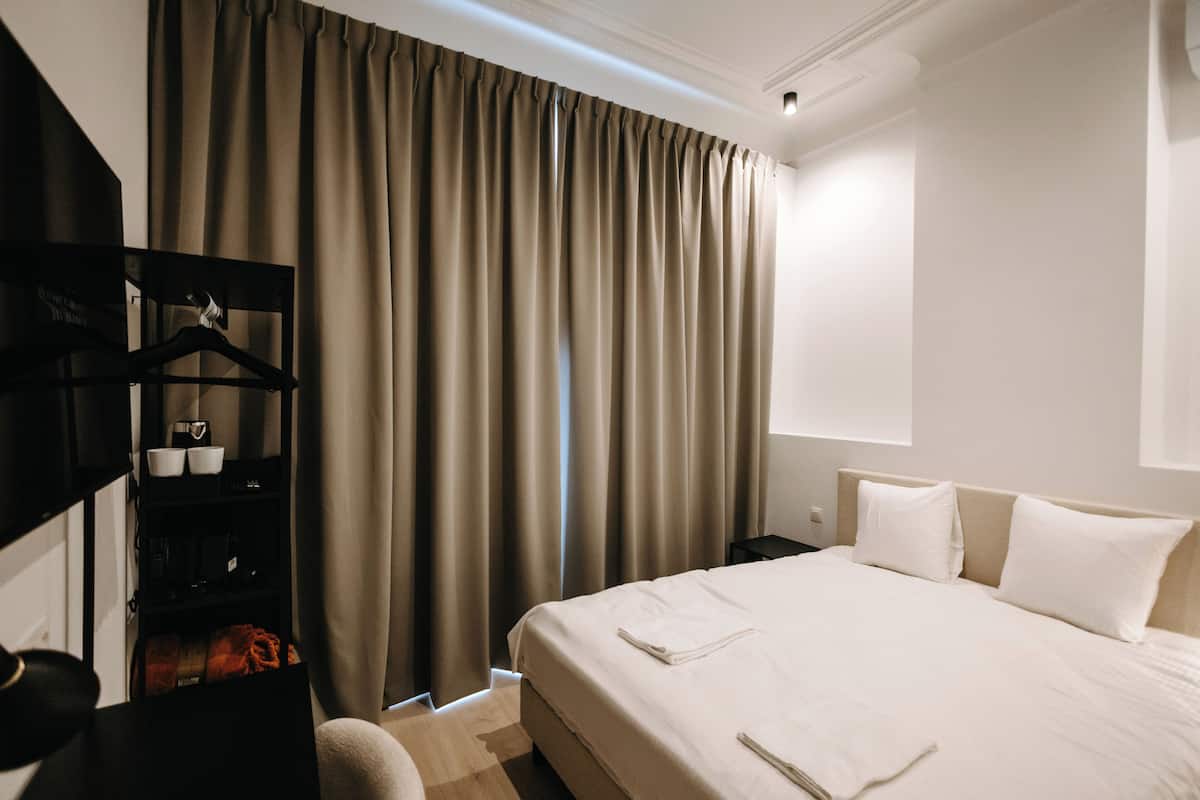 Une chambre d’hôtel avec un lit, une armoire, une table de chevet et une fenêtre avec des rideaux.