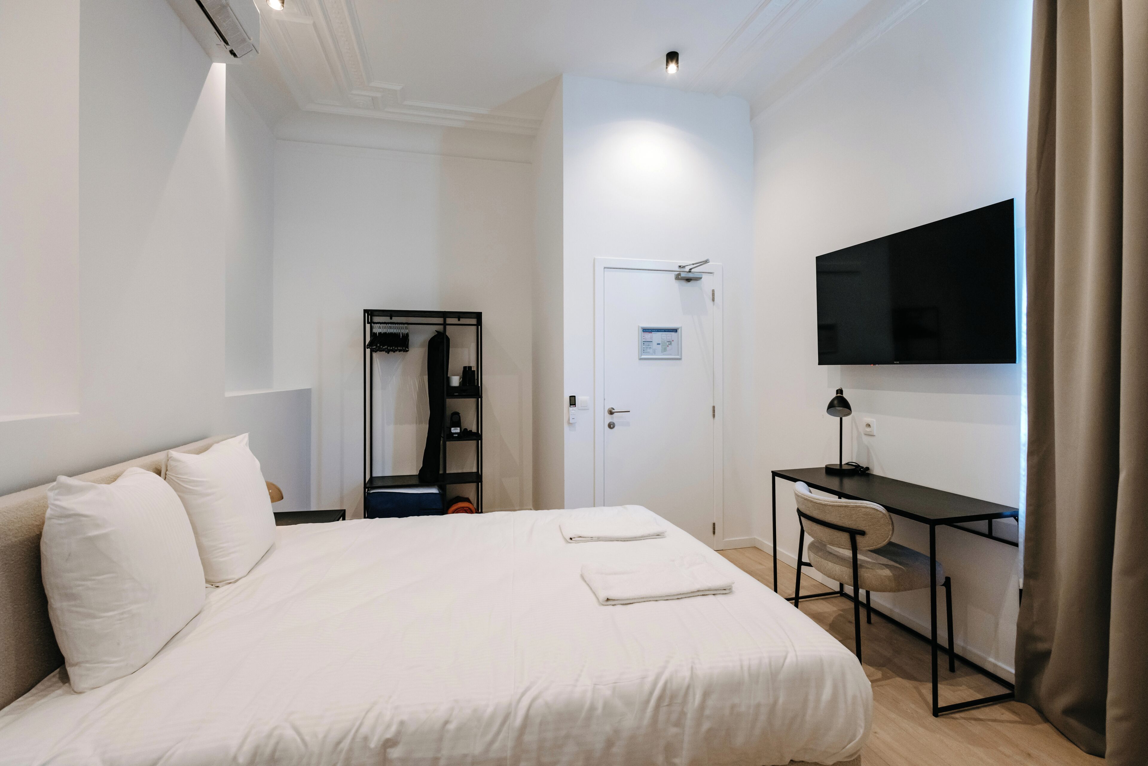 A hotel room with a bed, a desk, a TV, a wardrobe, and a door.