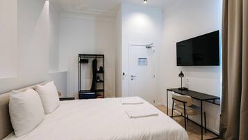 A hotel room with a bed, a desk, a TV, a wardrobe, and a door.