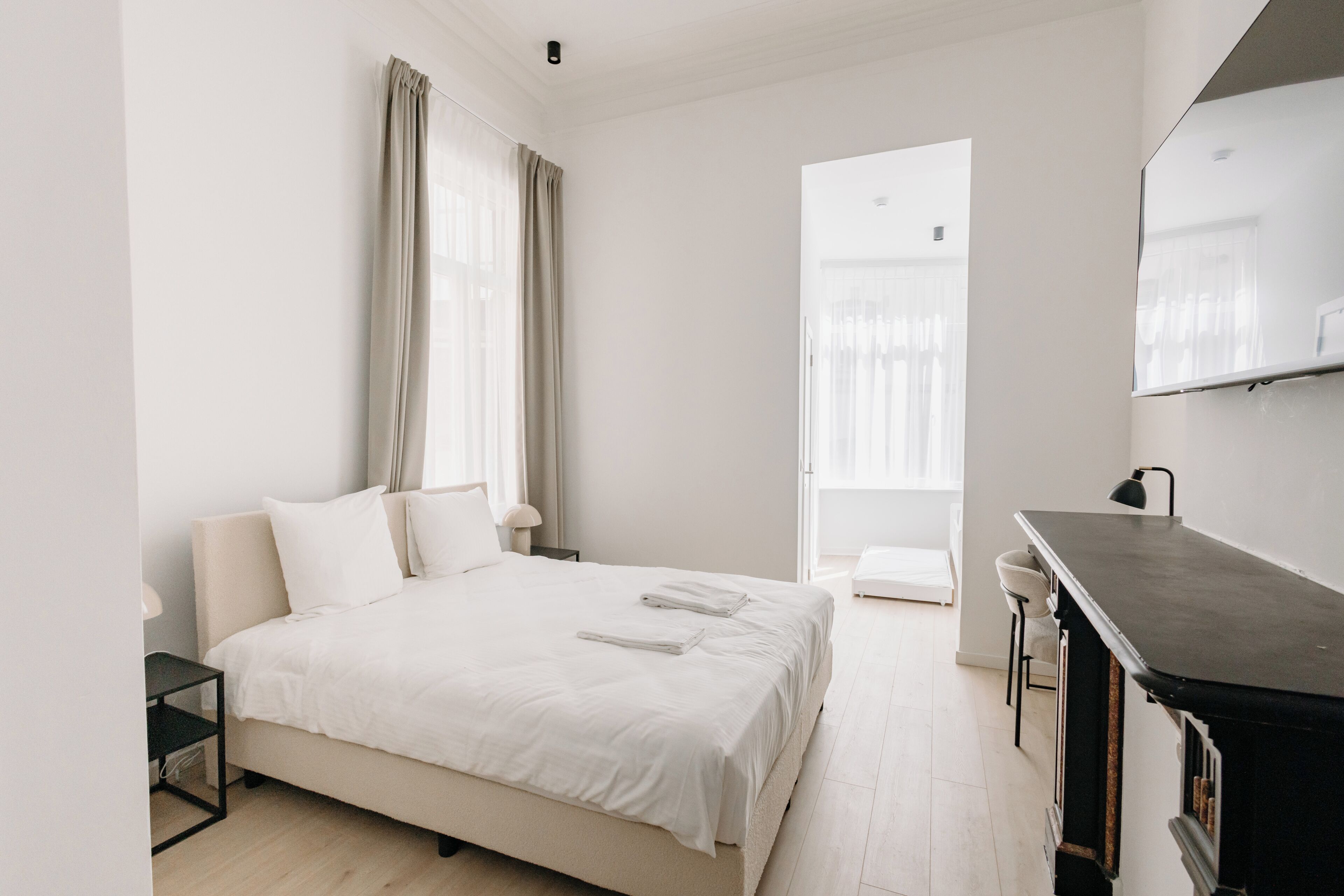 A modern hotel room with a large bed, a desk, and a view of the city.