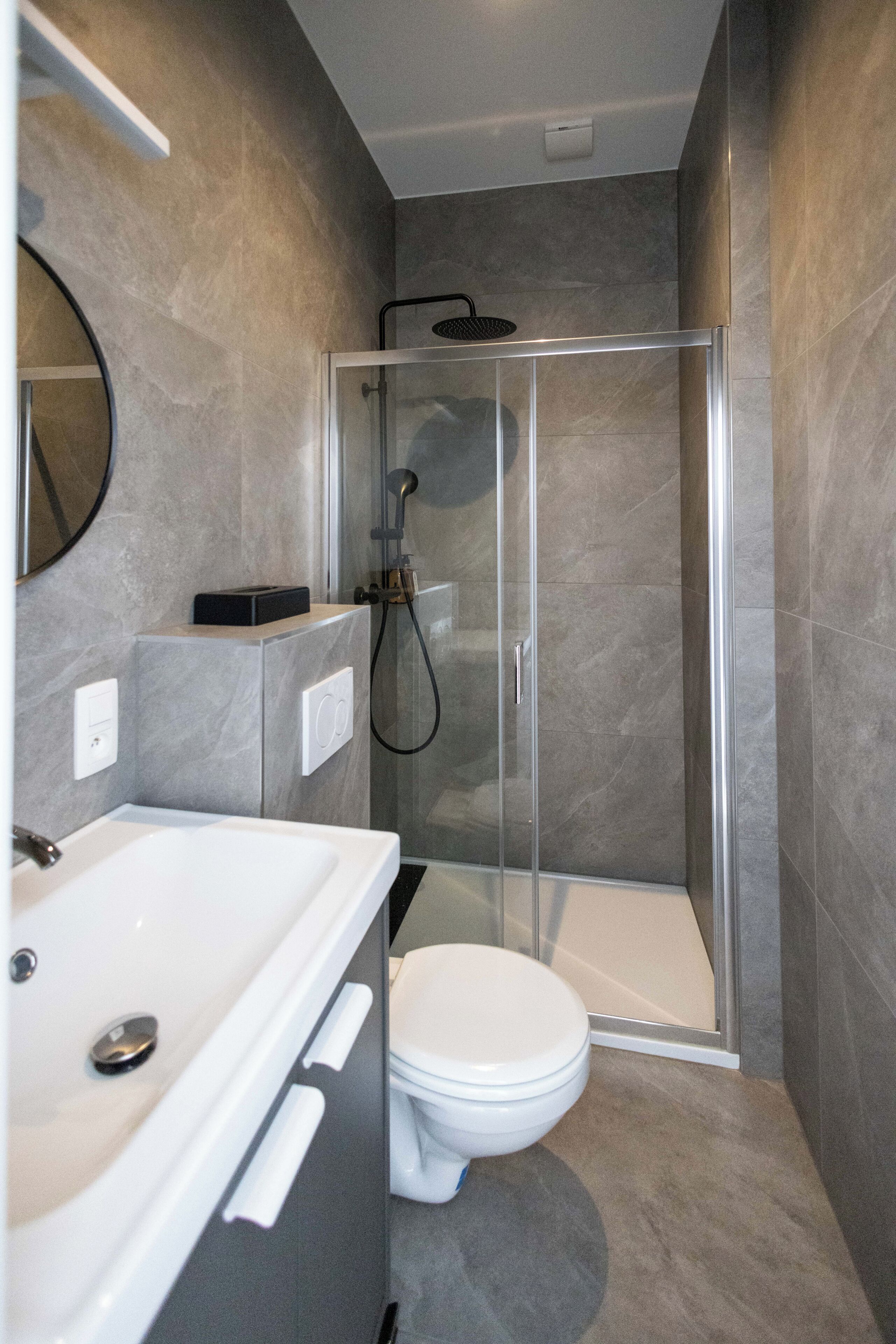 Een moderne badkamer met een douchecabine van glas, een witte wastafel en een toilet.