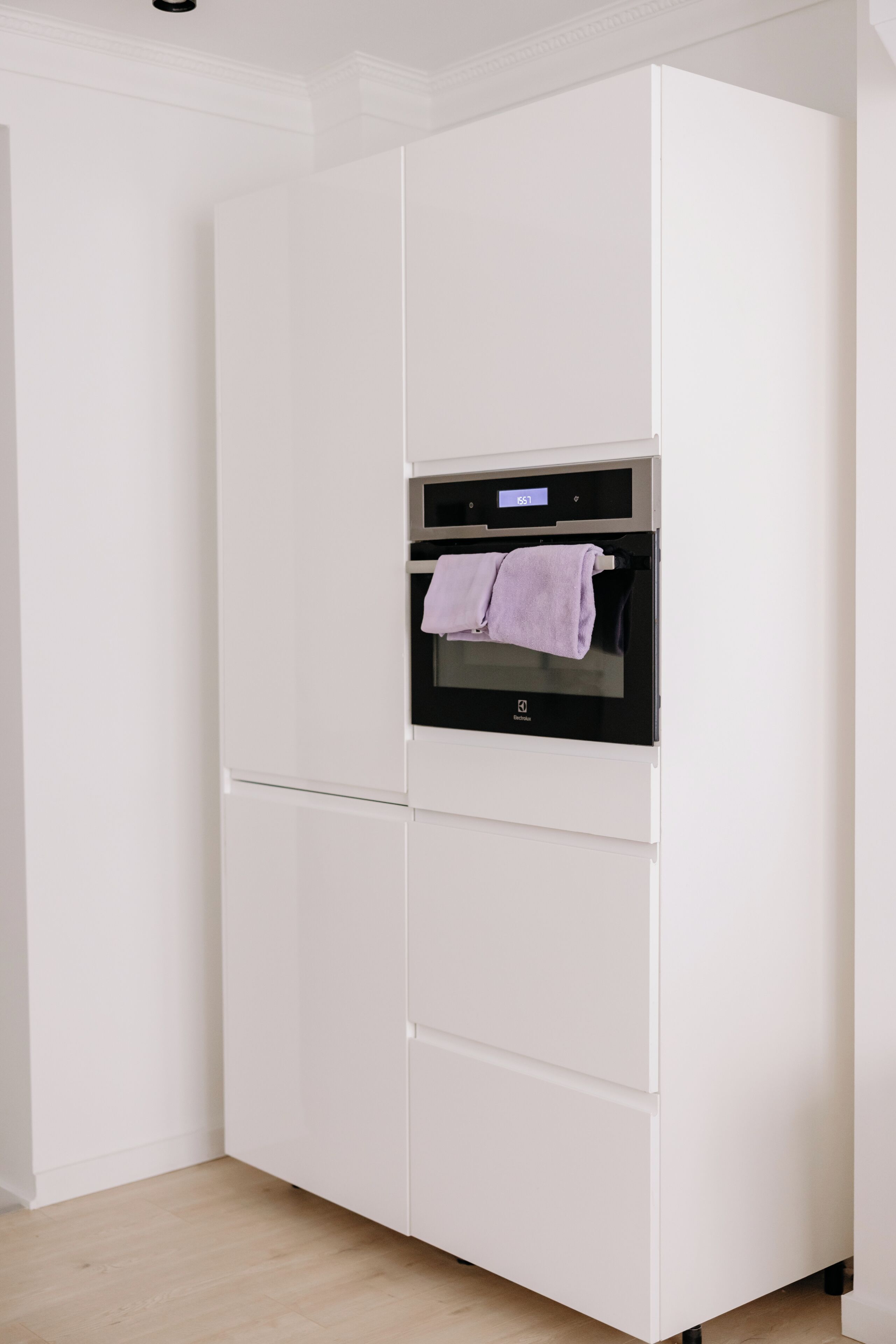 A white built-in oven with a digital display and a purple towel hanging on the door.