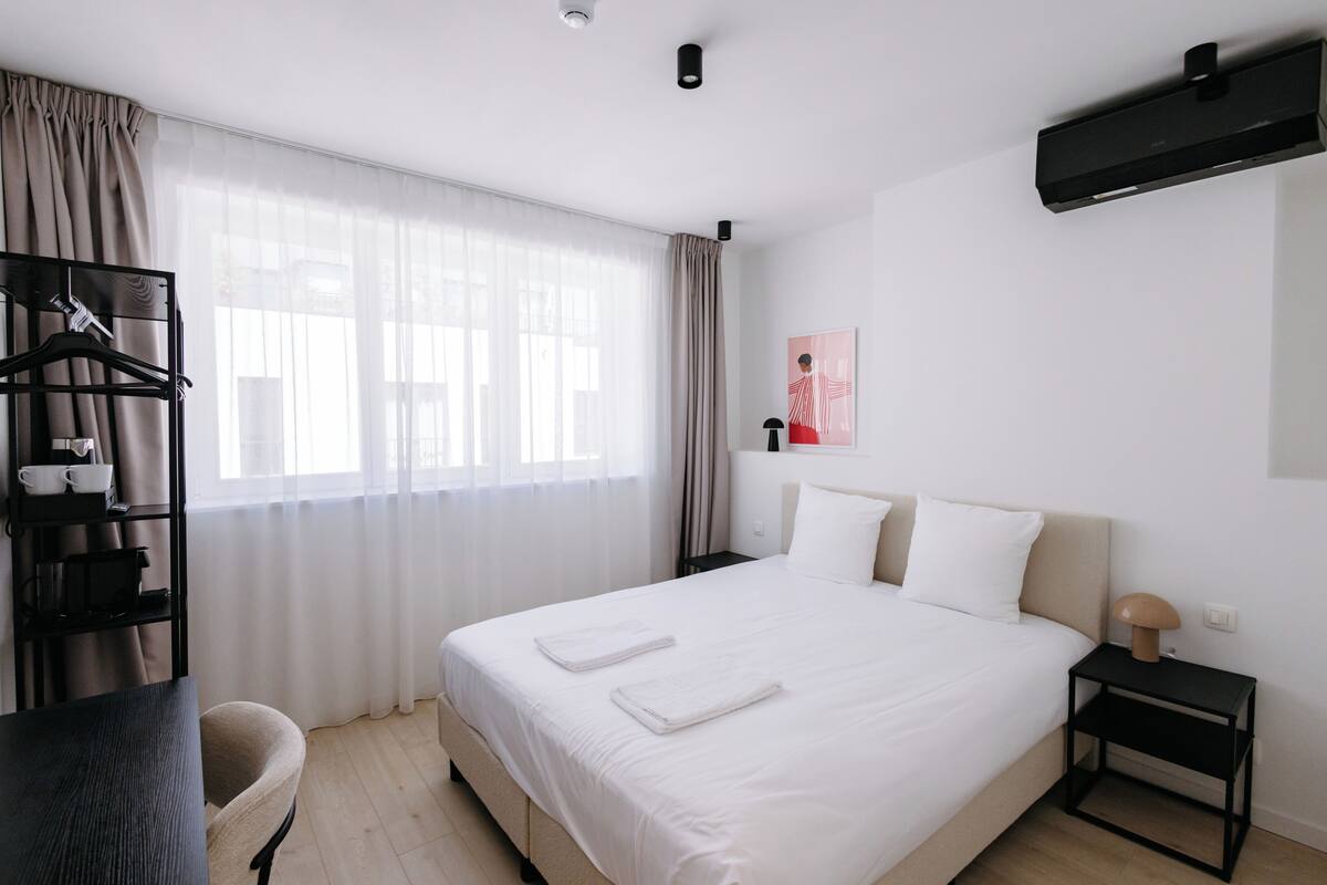 Une chambre d’hôtel équipée d’un lit, d’un bureau, d’une chaise, d’une armoire et d’une fenêtre avec des rideaux.