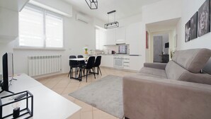 Una sala de estar moderna con sofá, una mesa de comedor con sillas, una zona de cocina y un ventanal grande.