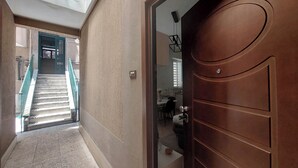 Un pasillo con una escalera que conduce a un segundo piso, una puerta de madera y una vista parcial de una cocina.