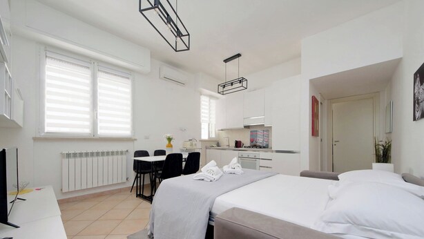 Una habitación de hotel moderna con cama, escritorio, silla, kitchenette pequeña y baño.