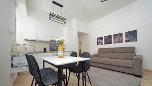 Una cocina moderna con armarios blancos, una mesa de comedor con cuatro sillas y un sofá gris en una sala de estar.