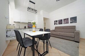 Eine moderne Küche mit weißen Schränken, einem Esstisch mit vier Stühlen und einem grauen Sofa im Wohnbereich.