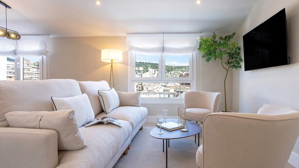 Ein modernes Wohnzimmer mit einer Couch, Sesseln, einem Couchtisch, einem Fernseher und einem Fenster mit Blick.