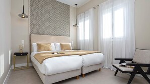 Ein ordentlich eingerichtetes Schlafzimmer mit einem Bett, Nachttischen, einem Sessel und einer Wand mit Muster.