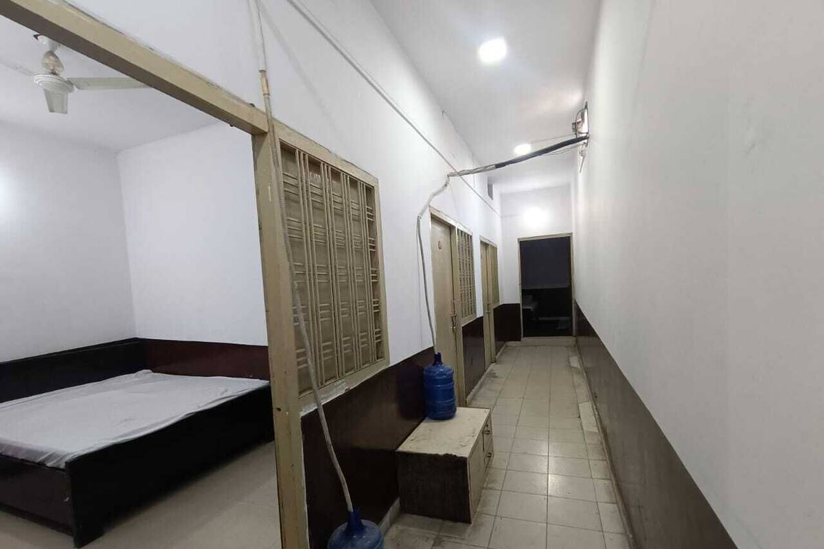 A corridor with a bed on the left, a window with bars, a water dispenser, and a door at the end.