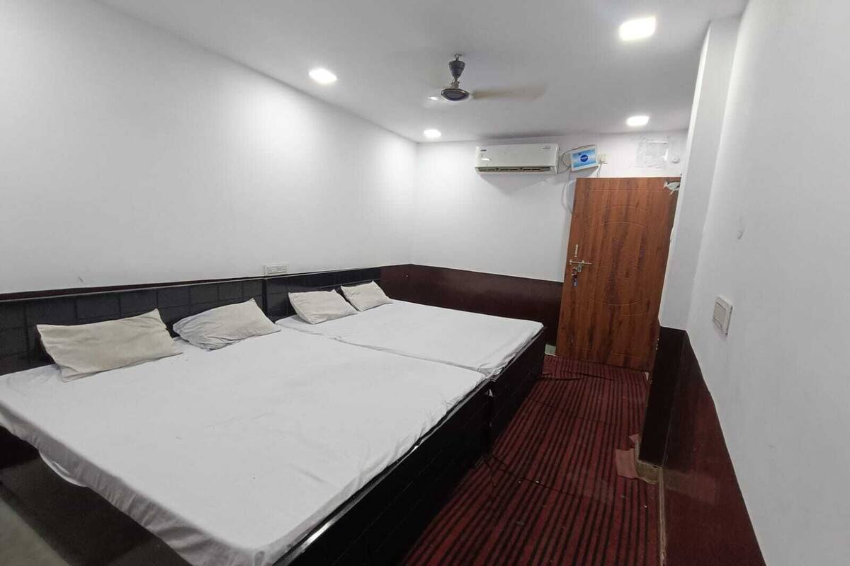 A hotel room with a bed, a ceiling fan, an air conditioning unit, and a door.