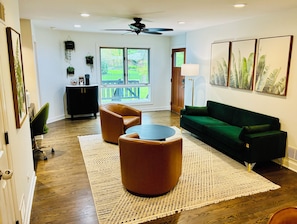 A modern living room with a green sofa, two leather armchairs, a round coffee table, a black cabinet, and a large window with a view of a backyard. - Cozy Fully Furnished 5B4B Palos Heights Oasis (Palos Heights)