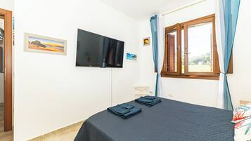 Ein Schlafzimmer mit Bett, Wandfernseher, Fenster mit Vorhängen und einem kleinen Tisch.