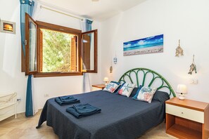 Ein Schlafzimmer mit Bett, einem Fenster mit Vorhängen, einem Nachttisch, einem Wandbild und einem dekorativen Gegenstand.