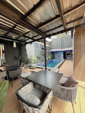 Un patio exterior con piscina, mobiliario cubierto y vistas al área de la piscina.