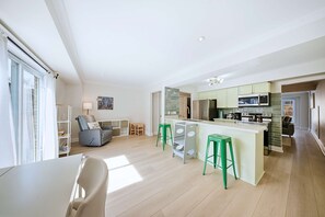 Eine moderne Küche mit einer zentralen Kochinsel, grünen Barhocker und einem Essbereich mit Tisch und Stühlen.