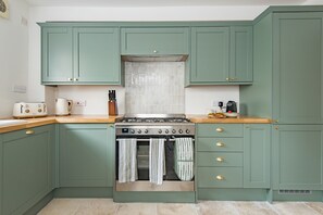 A kitchen with teal cabinets, a stove, and a tiled backsplash. - The Tide House, Broadstairs (Broadstairs)