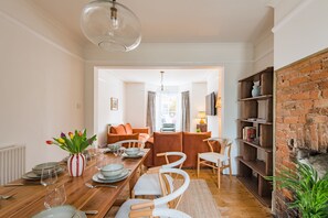 A dining area with a wooden table, chairs, and a vase of tulips. There is a brick wall and a fireplace in the background. - The Tide House, Broadstairs (Broadstairs)