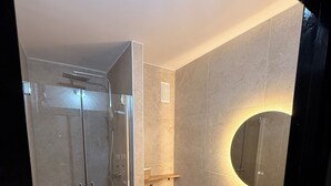 Een moderne badkamer met een glazen douchecabine, een toilet, een wastafel met spiegel en een klein plankje.